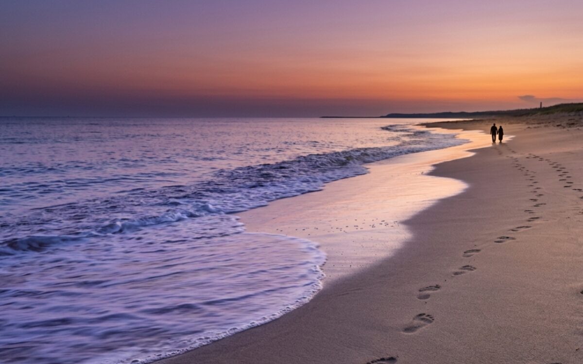 夕暮れの静かな海辺。波打ち際に残された、寄り添う二人の足跡と新しい始まり。